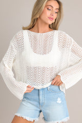 Full front view of this top that features a high rounded neckline, a soft material, an open-knit crochet design, scalloped long sleeves, and a scalloped hemline.