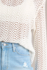 Close up view of this top that features a high rounded neckline, a soft material, an open-knit crochet design, scalloped long sleeves, and a scalloped hemline.