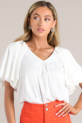 Close up view of an ivory blouse with a v neckline and puff sleeves.
