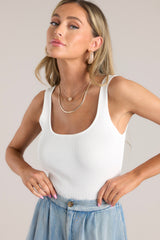 This white bodysuit features a scoop neckline, an open back, a ribbed material, and snap button closures at the bottom.