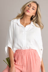 This white top features a collared neckline, functional buttons, dolman sleeves, and an oversized fit.