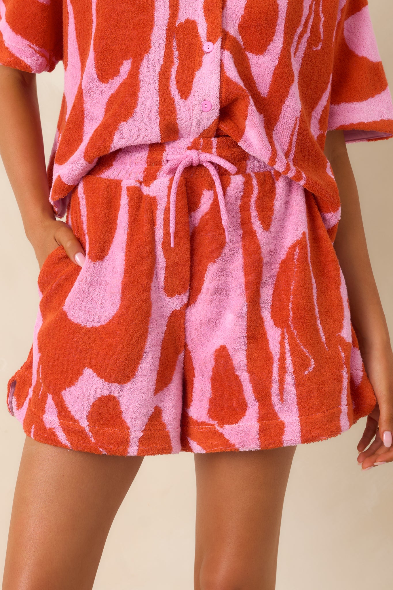 Detailed view of textured fabric showing bold pink and red abstract floral print with elastic waistband and drawstring ties.