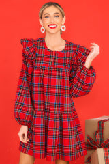 Front view of this dress that features a round neckline, three functional buttons down the front, ruffle detailing on the shoulders, long sleeves with elastic cuffs, and a babydoll silhouette.
