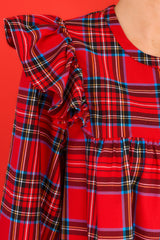 Close up view of this dress that features a round neckline, three functional buttons down the front, ruffle detailing on the shoulders, long sleeves with elastic cuffs, and a babydoll silhouette.