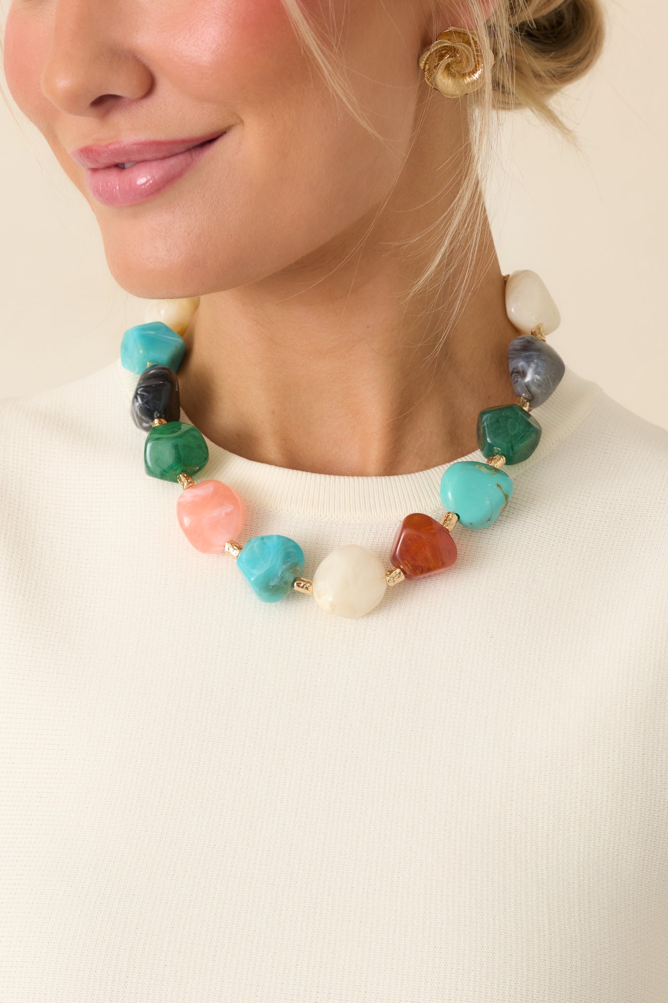 Close cropped angle of structured chain necklace highlighting mixed hue stones and polished gold detailing.