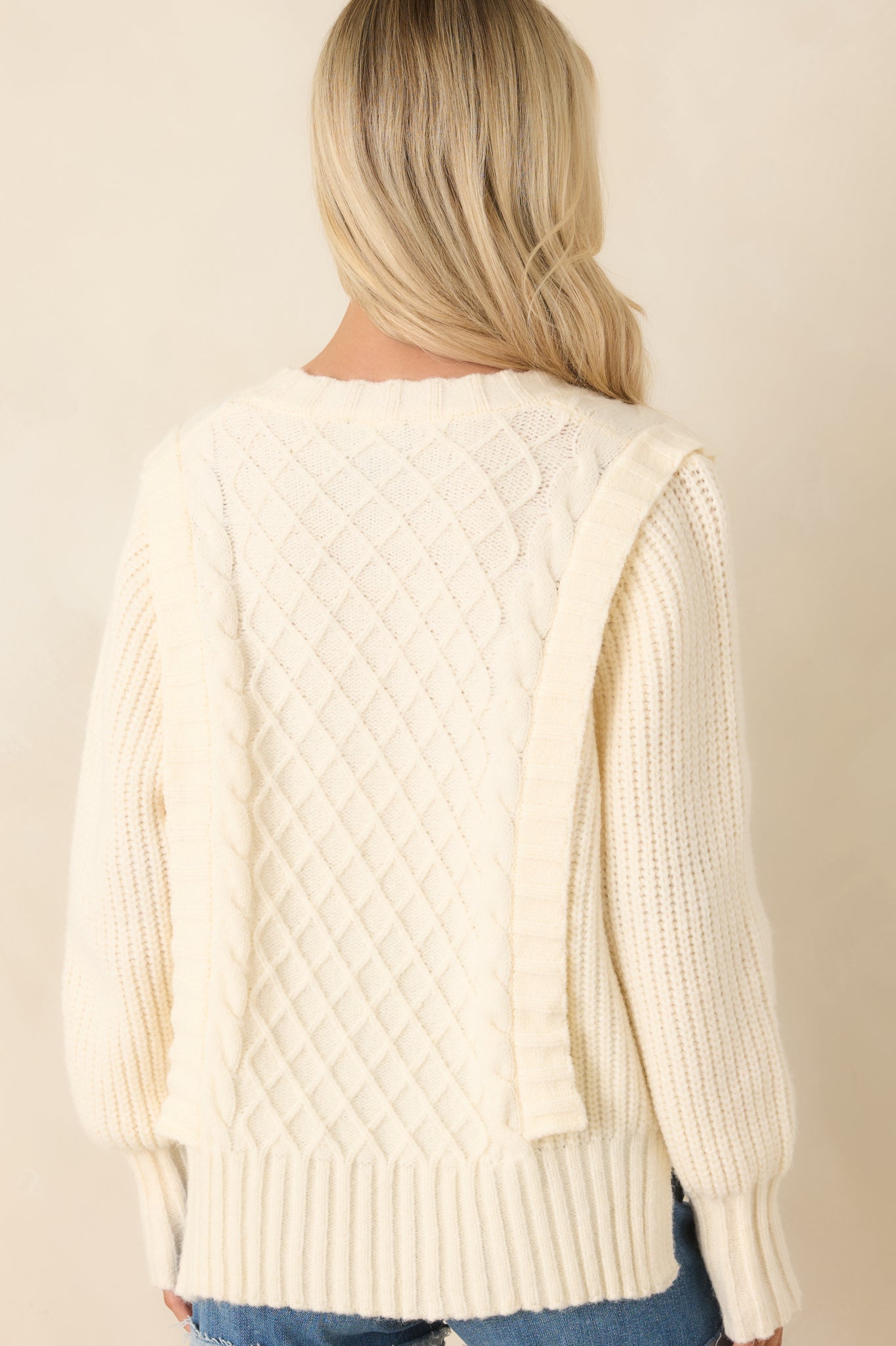 Rear view of ivory V-neck knit sweater with continuous textured panel detailing and ribbed trim.