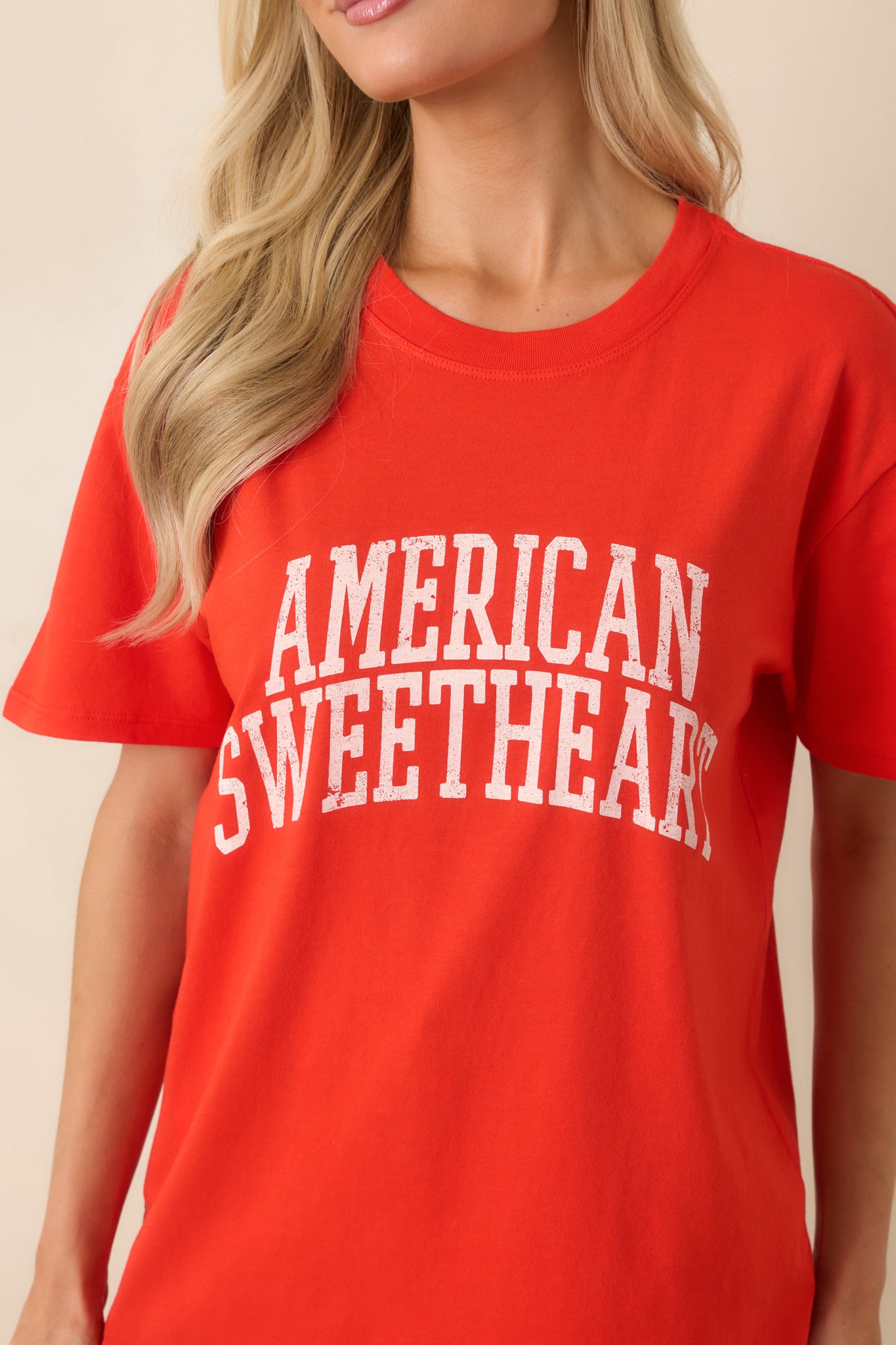 Detailed view of the distressed front lettering on the soft poppy red cotton tee fabric.