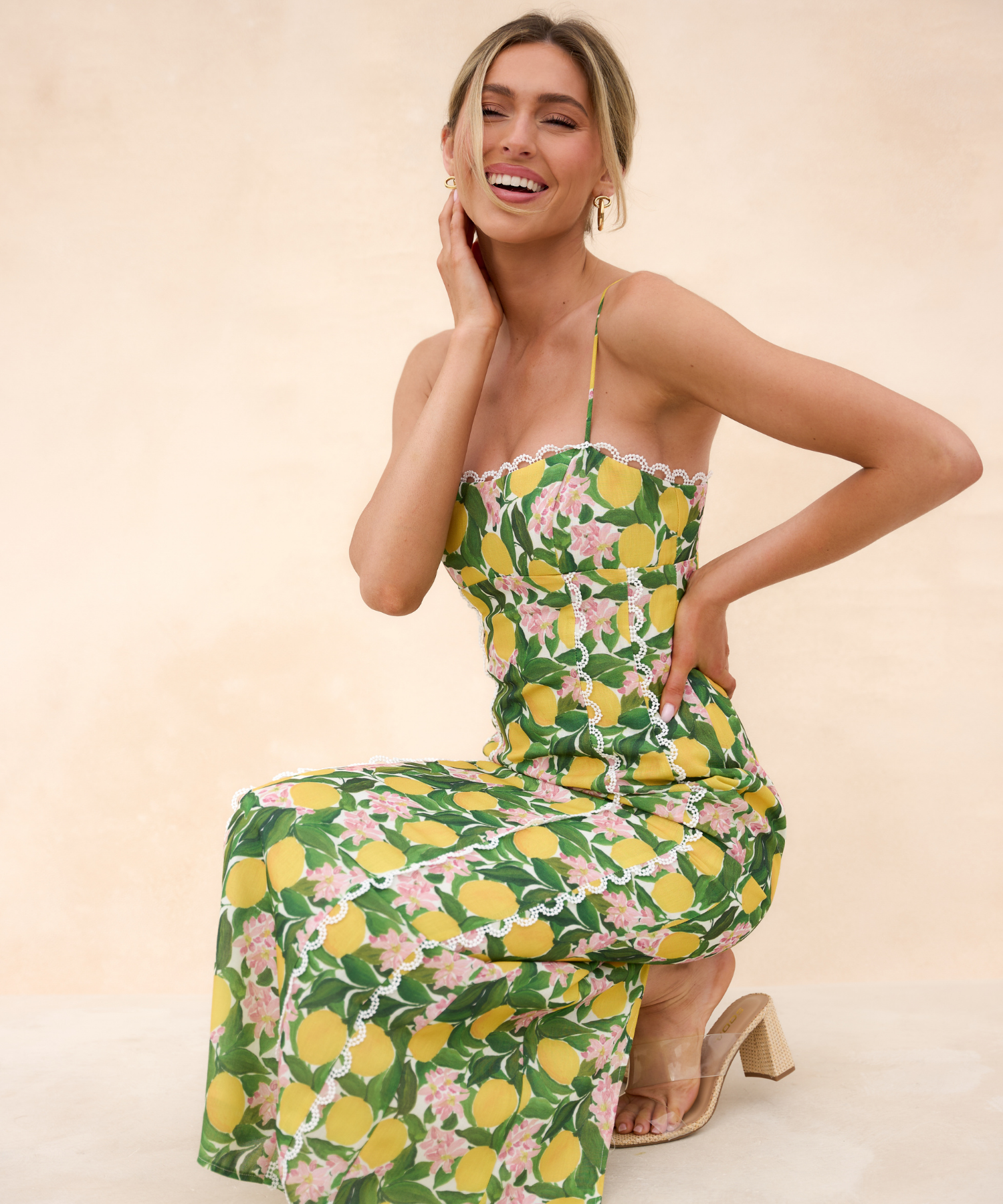 Woman squatting down in a lemon and floral print maxi dress against a beige background.