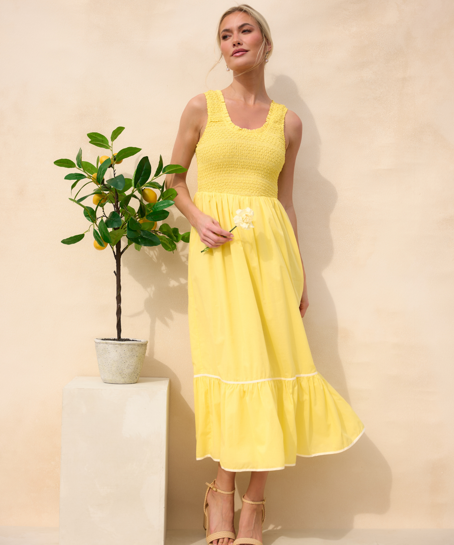 Woman wearing a yellow dress next to a small lemon tree.