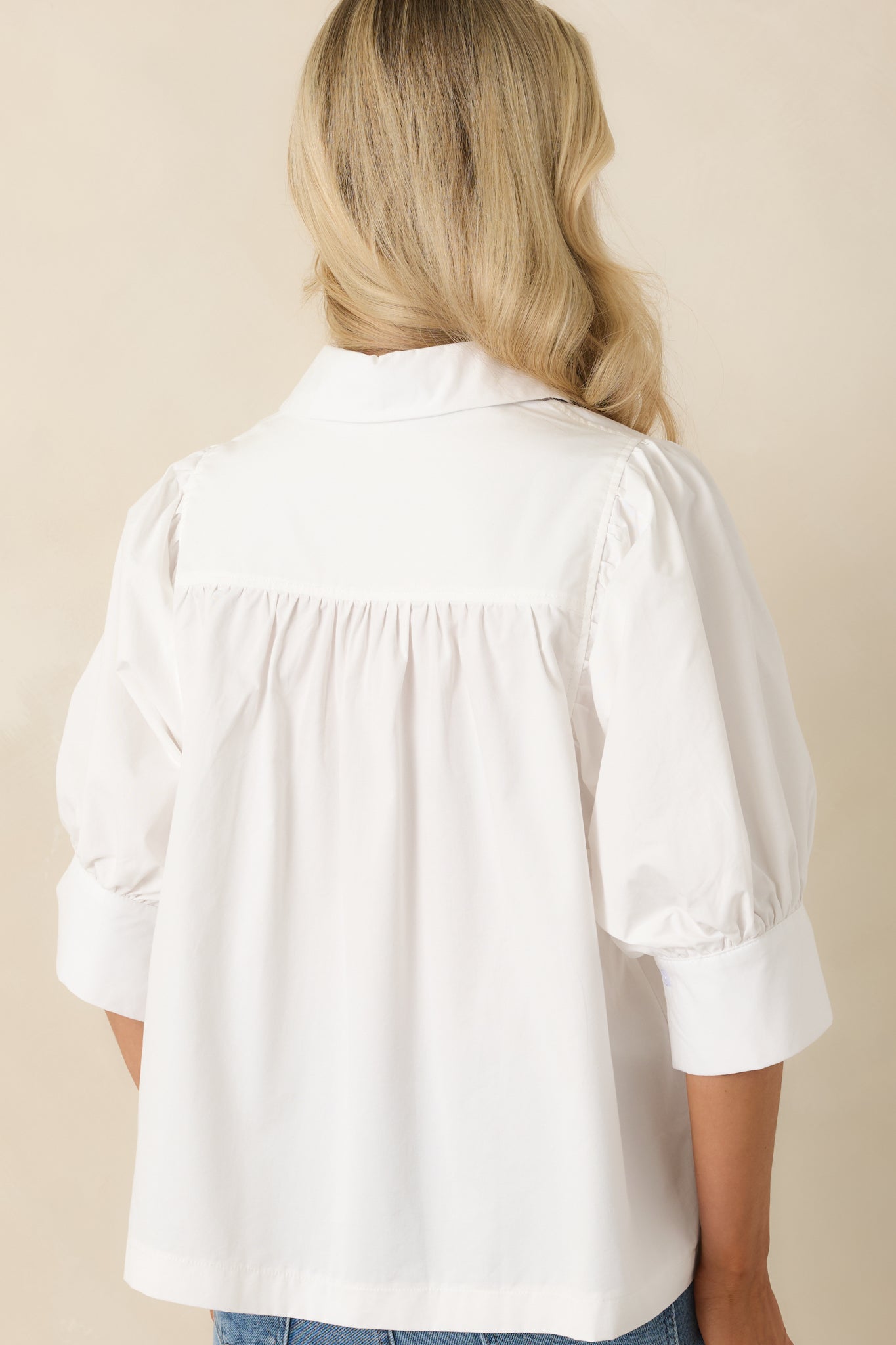 Back view of the white cotton top highlighting the gathered back yoke, relaxed silhouette, and short puff sleeves with wide cuffs.