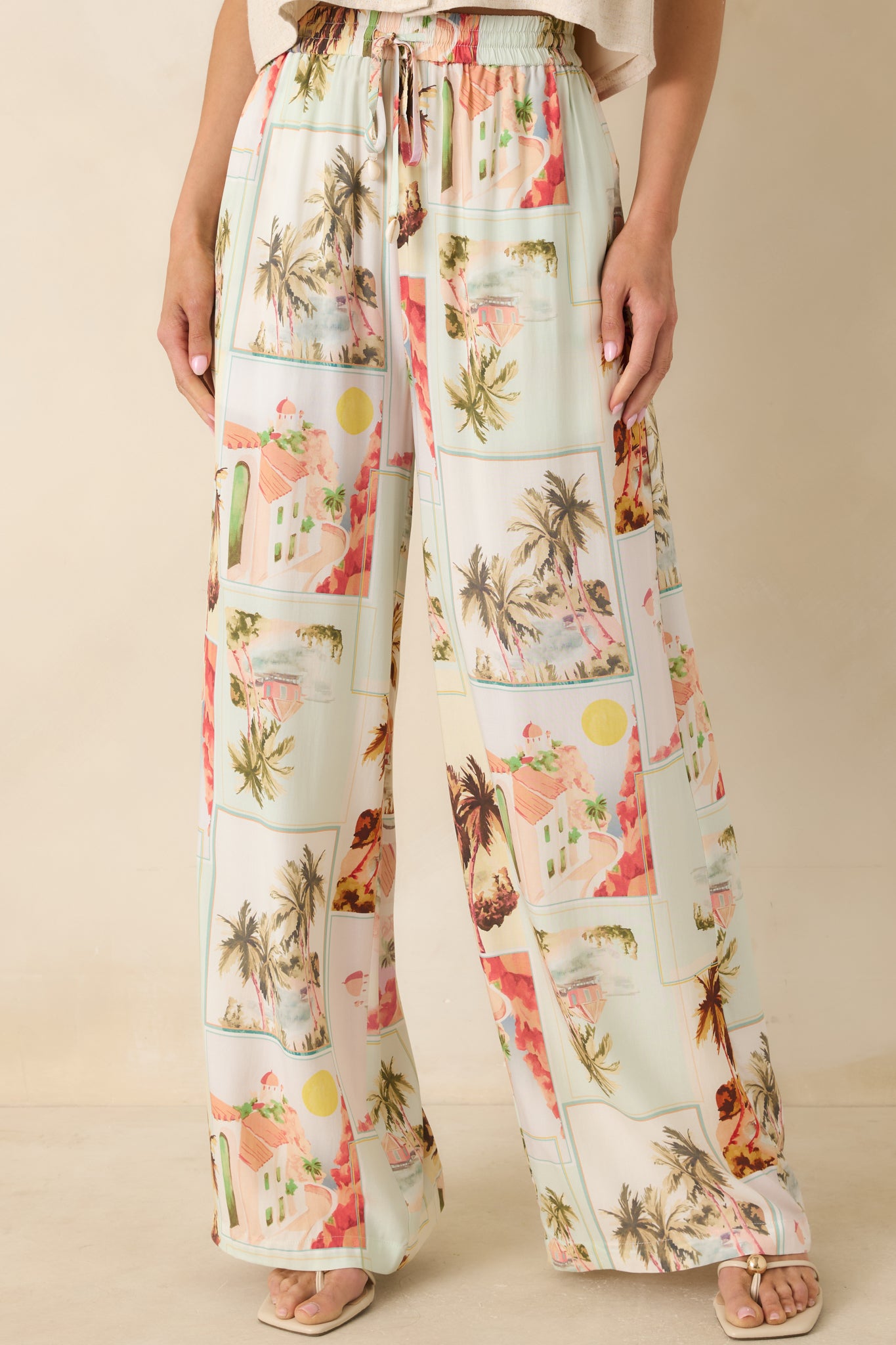 Cropped view of postcard print pants highlighting the palm tree motifs and warm, sun-washed color palette