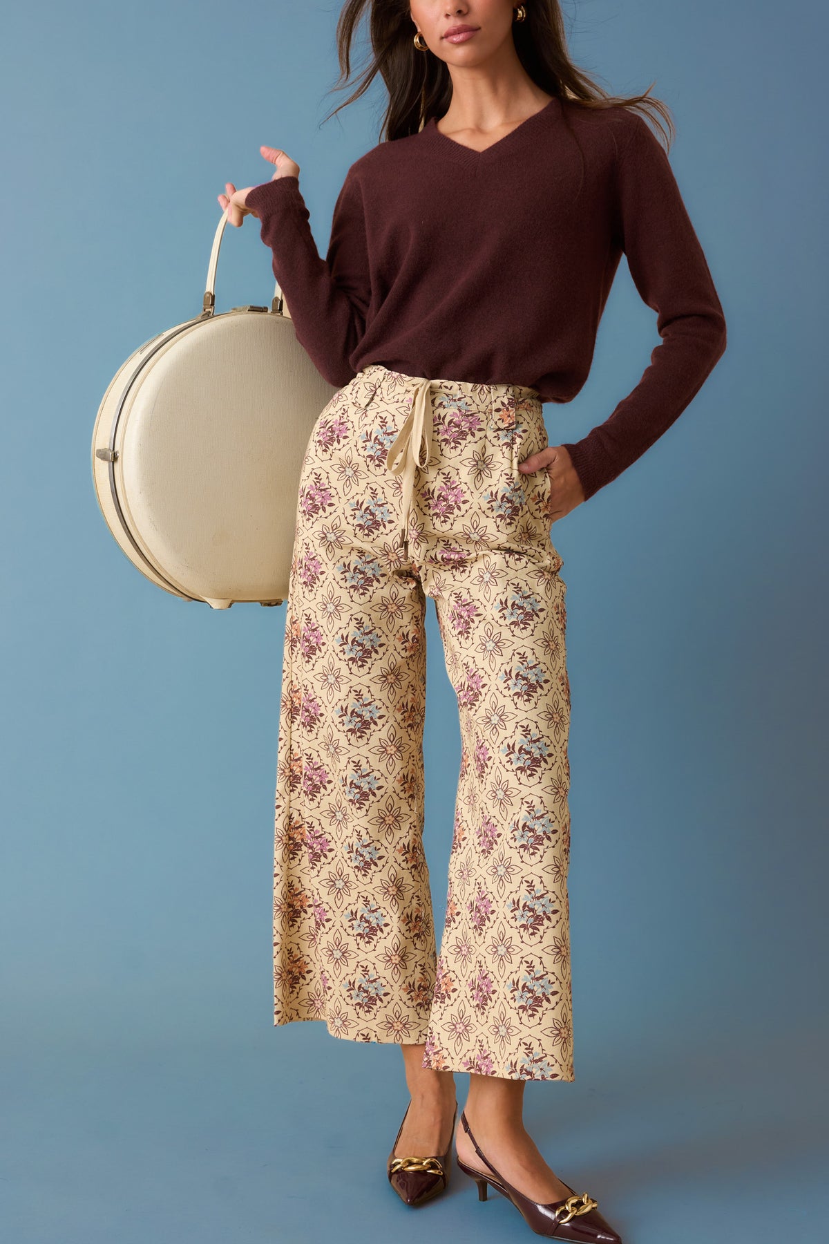 Woman wearing cream pants with a multi color floral geometric print against a faded blue backdrop. 