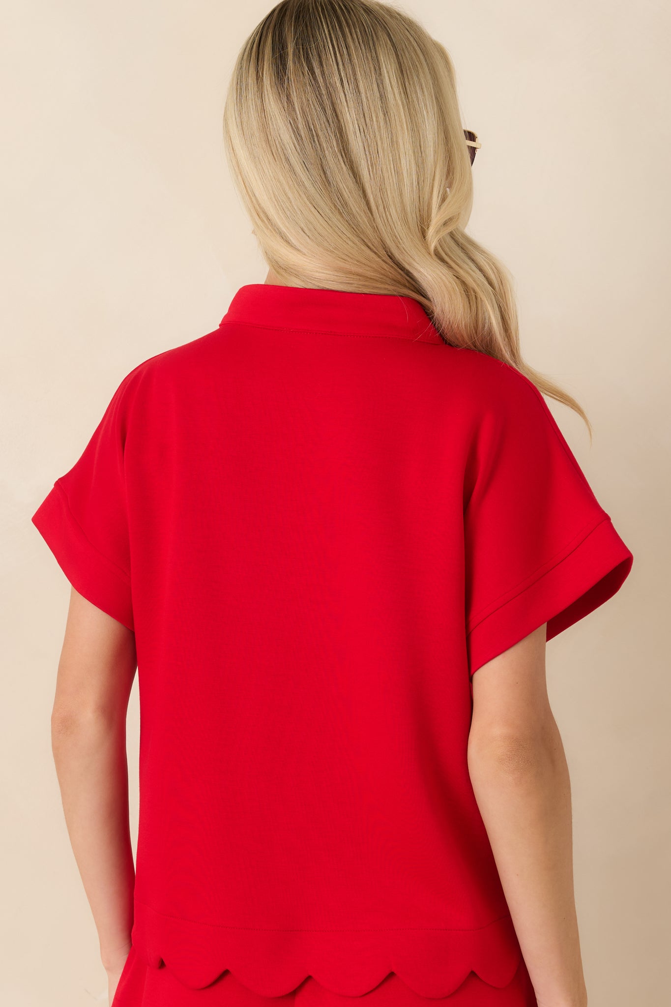Rear view of the red top displaying the relaxed fit, short sleeves, and scalloped hem detail.