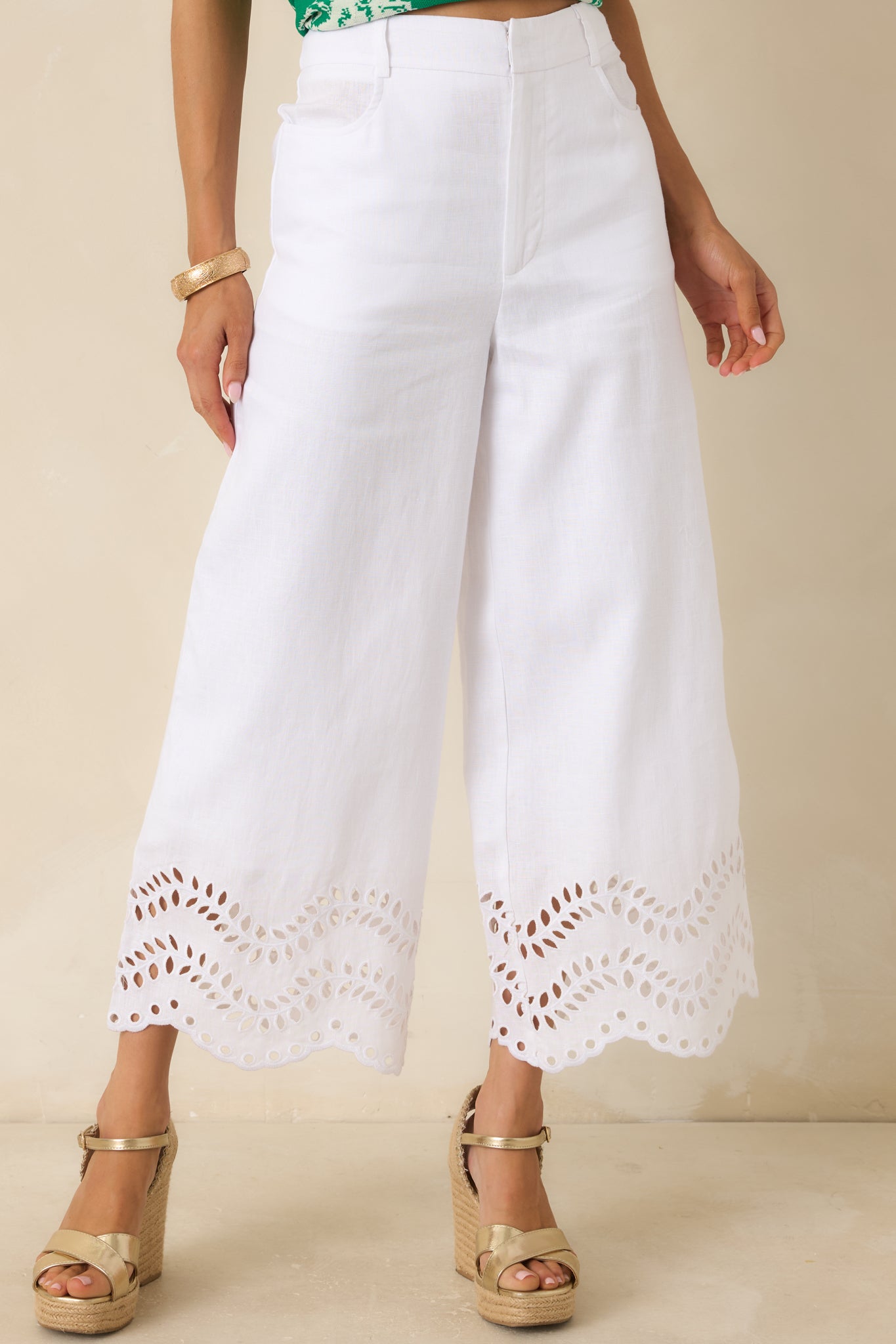 Close view of the eyelet scalloped hem detailing on the white wide leg pants.