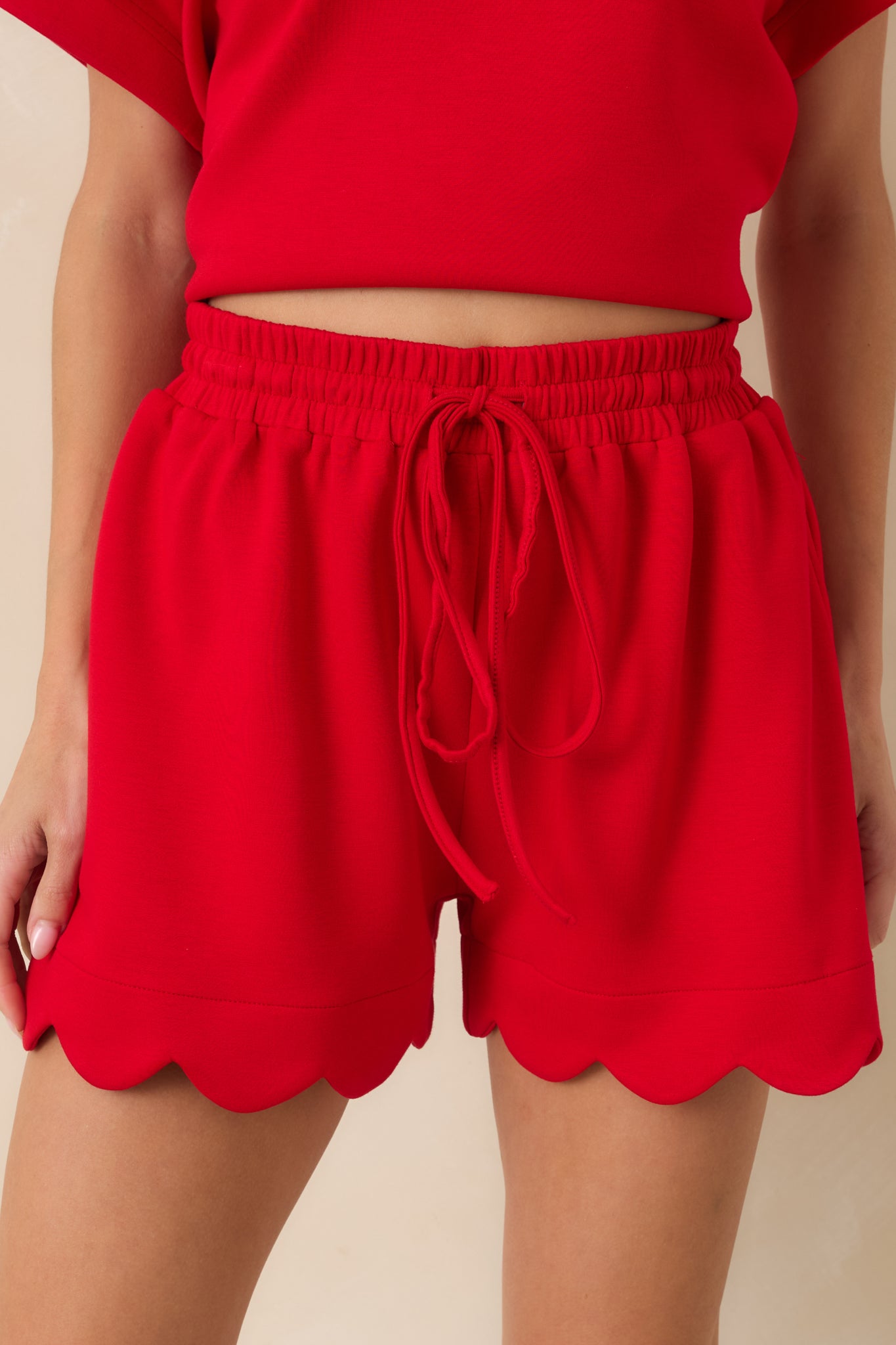 Close-up of red shorts featuring the gathered elastic waistband, drawstring tie, and smooth fabric texture.
