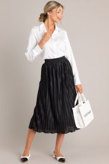 Styled view of this black skirt featuring a high-waisted fit, an elastic waistband, shiny material, and a pleated design.