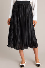 Black skirt featuring a high-waisted fit, an elastic waistband, shiny material, and a pleated design.