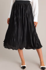 Front view of a black skirt featuring a high-waisted fit, an elastic waistband, shiny material, and a pleated design.