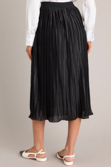 Back view of a black skirt featuring a high-waisted fit, an elastic waistband, shiny material, and a pleated design.