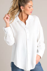This all ivory top features a collared neckline, dropped shoulders, functional buttons down the front, and buttoned cuffed long sleeves.