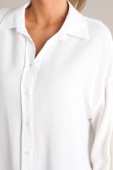 Close up view of this ivory top that features a collared neckline, dropped shoulders, functional buttons down the front, and buttoned cuffed long sleeves.