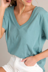 Close up view of this green top that features a v-neckline, short sleeves, and a lightweight fabric.