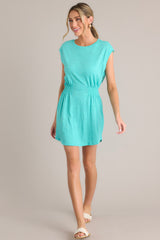 This green dress features a crew neckline, smocking in the waist, a textured material, and a vibrant color.