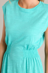 Close up view of this dress that features a crew neckline, smocking in the waist, a textured material, and a vibrant color.