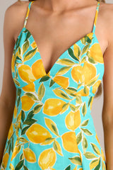 Close up view of this aqua midi dress that features a v-neckline, thin adjustable straps with a self-tie feature, an open back with functional buttons, functional hip pockets, and, a vibrant aqua lemon print.