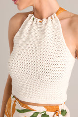 Close up view of this beige top that features a halter neckline, a knitted material, self-tie straps that cross in the back, and a cropped hemline.