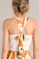 Back view of this beige top that features a halter neckline, a knitted material, self-tie straps that cross in the back, and a cropped hemline.