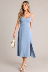 Full body view of this ash blue midi dress that features a v-neckline, thin adjustable straps, a smocked back insert, gathering in the bust, a thick waistband, and a side slit.