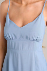 Close up view of this ash blue midi dress that features a v-neckline, thin adjustable straps, a smocked back insert, gathering in the bust, a thick waistband, and a side slit.