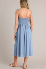Back view of this ash blue midi dress that features a v-neckline, thin adjustable straps, a smocked back insert, gathering in the bust, a thick waistband, and a side slit.