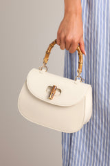 This white handbag features a single flap design, a bamboo top handle, a bamboo twist lock closure, and a removable strap.