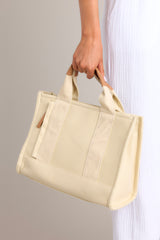 A close up view of this canvas bag that features gold hardware, top handles, a functional zipper closure, an additional pocket on the inside, and a removable strap.