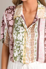 Close up view of this shirt that features a collared neckline, functional buttons down the front, an abstract pattern, and a cropped length. 