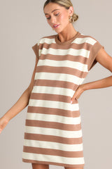 Angled front view of this light brown stripe mini dress that features a crew neckline, wide cap sleeves, functional hip pockets, and a relaxed fit.