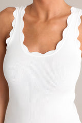 Close up view of the neckline of this ivory tank top with a scalloped scoop neckline, thick scalloped straps, ribbed texture, and a bodycon fit