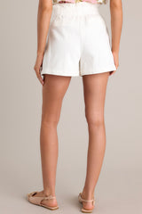 Back view of these ivory shorts that feature a high waisted paper bag design, an elastic waistband, a zipper closure, functional hip pockets, and faux back pockets.