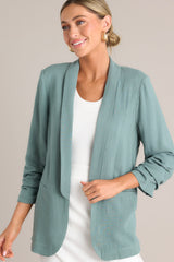 A forest green blazer with a folded neckline, shoulder padding, faux pockets, and gathered quarter-length sleeves.