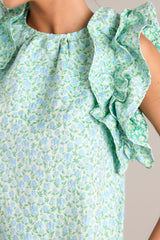 Close up view of the pattern of this light green dress that features a high crew neckline, a unique floral pattern, functional hip pockets, and ruffled sleeves.
