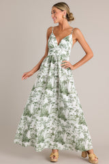 Angled front view of this green toile maxi dress that features a v-neckline, thin adjustable straps, a slightly pleated bust, a smocked back insert, a thick waistband, and a flowing silhouette.