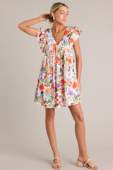 Full body front view of this ivory mini dress with v-neckline, bust gathering, flowing silhouette, floral pattern, short ruffled flutter sleeves.