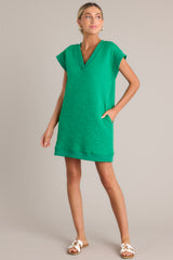 Angled front view of this green mini dress that features a v-neckline, an all over quilted design, functional hip pockets, and flattering cap sleeves.