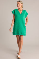 Full body view of this green mini dress that features a v-neckline, an all over quilted design, functional hip pockets, and flattering cap sleeves.