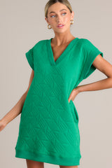 Angled close up view of this green mini dress that features a v-neckline, an all over quilted design, functional hip pockets, and flattering cap sleeves.