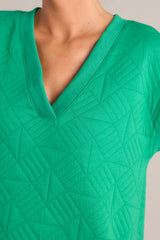 Close up view of this green mini dress that features a v-neckline, an all over quilted design, functional hip pockets, and flattering cap sleeves.