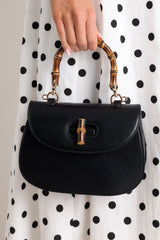 Close up view of this black handbag that features a single flap design, a bamboo top handle, a bamboo twist lock closure, and a removable strap.