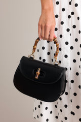 This black handbag features a single flap design, a bamboo top handle, a bamboo twist lock closure, and a removable strap.